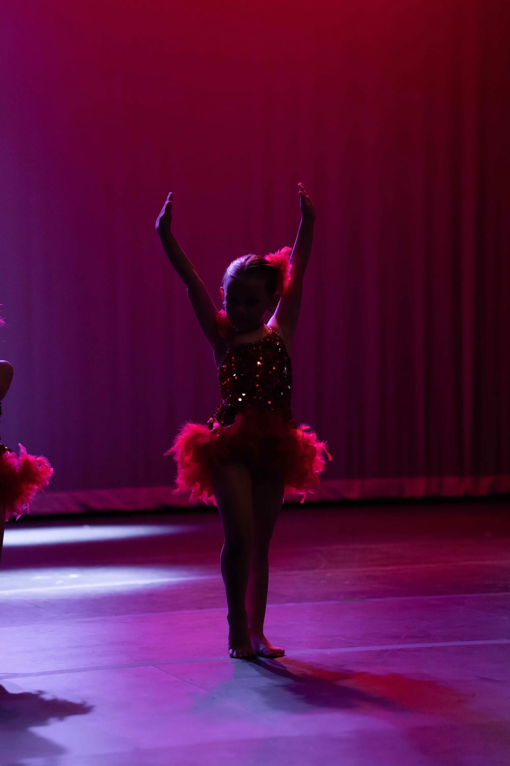 Young dancer with red and purple lighting with her hands raised